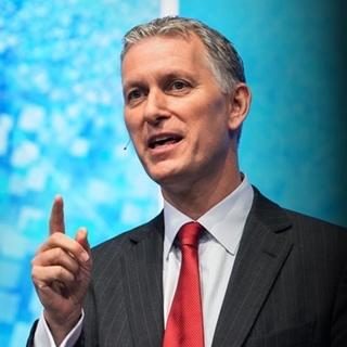 Peter Sondergaard in a suit and tie pointing up